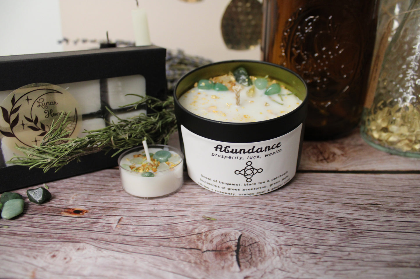 Candle in a black container labeled 'Abundance' on a wooden surface with decorative items.