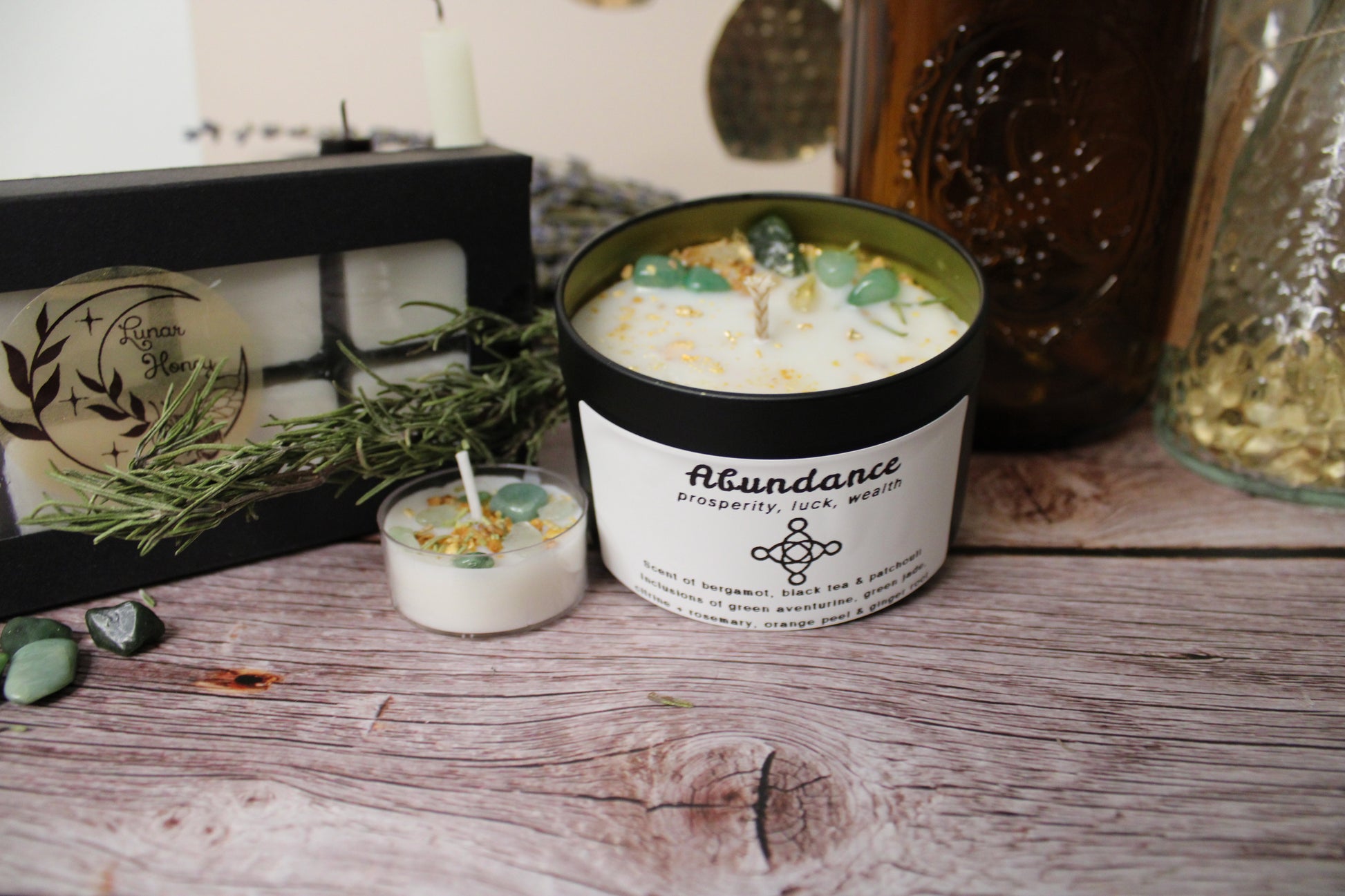 Candle in a black container labeled 'Abundance' on a wooden surface with decorative items.